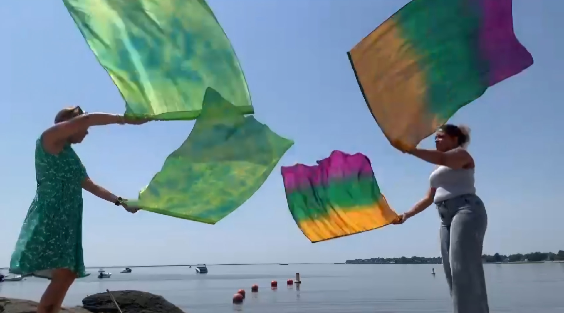 Two worshippers waving large colorful silks by the shoreline