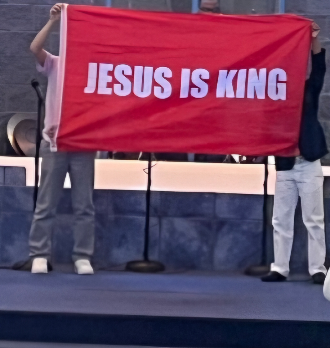Students holding a red 'Jesus is King' banner on stage
