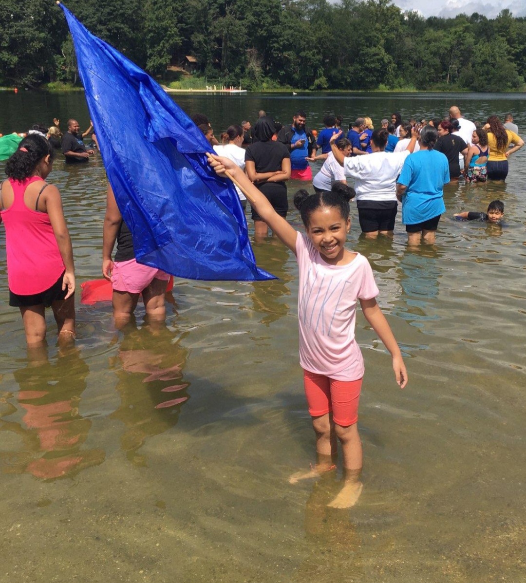 Young girl waving a blue flag in the lake during a baptism gathering